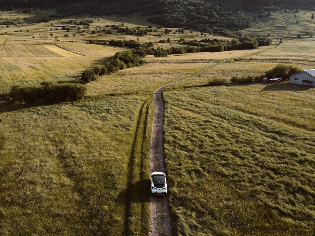 Elektrische auto op een landweggetje in een heuvelachtig landschap.